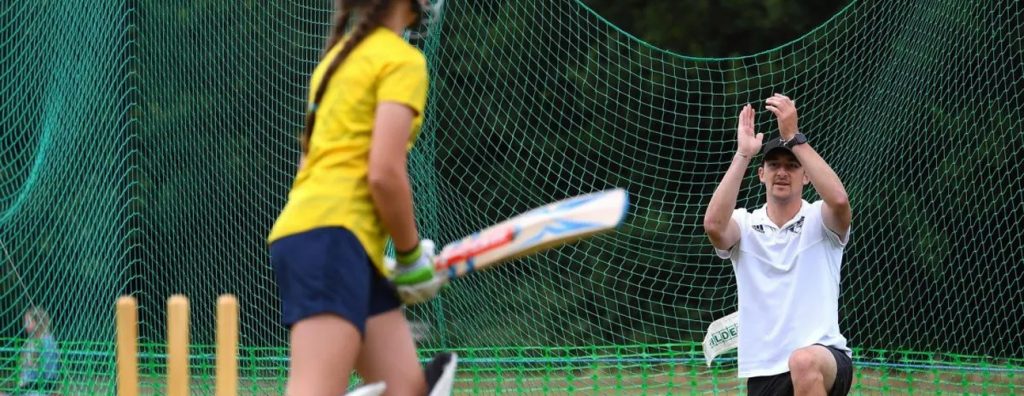 girl and cricket coach playing cricket in nets